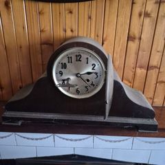vintage mechanical mantel clock, styled in a traditional "Napoleon hat" or humpback tambour shape with a dark wooden case.