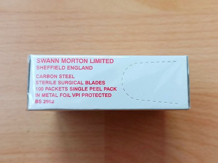 Box of Swann-Morton carbon steel sterile surgical blades manufactured in Sheffield, England, containing 100 individually foil-peel-packed blades protected with VPI