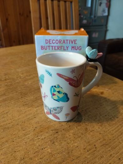 Butterfly Shaped Handle Ceramic Mug, decorated with various colorful butterfly graphics. 3D ceramic butterfly molded directly onto the handle. New in Box.