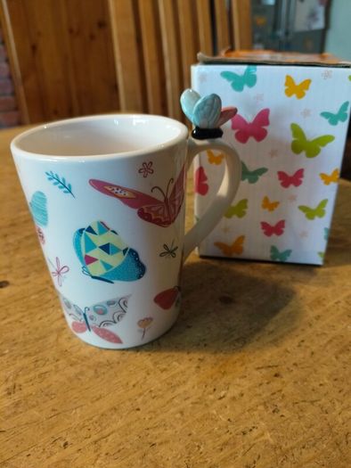 Butterfly Shaped Handle Ceramic Mug, decorated with various colorful butterfly graphics. 3D ceramic butterfly molded directly onto the handle. New in Box.