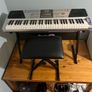 RockJam Electronic Keyboard Piano set up on a sturdy, matching heavy-duty Z-frame stand and an adjustable padded X-frame RockJam Keyboard Bench resting on a wooden surface. Image 5