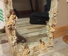 Rococo style wall mirror features a heavy, ornate resin frame decorated with carved cherubs and floral motifs