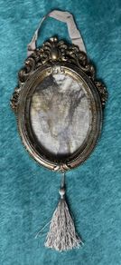 vintage-style oval picture frame in silver with a tassel and ribbon hanger