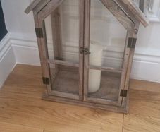 Rustic house-shaped wooden lantern featuring glass panel doors and a pitched roof design