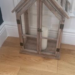 Rustic house-shaped wooden lantern featuring glass panel doors and a pitched roof design
