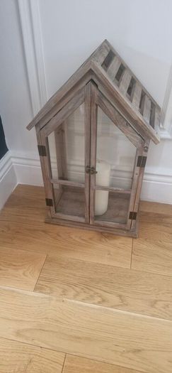 Rustic house-shaped wooden lantern featuring glass panel doors and a pitched roof design
